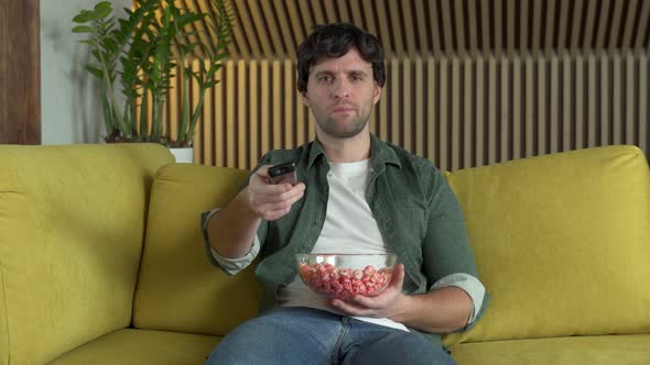 A Man in Front of the TV Watching a Sports Game or a Movie Sitting on a Yellow Sofa and Eating alt
