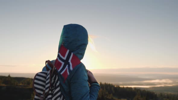 A Tourist with a Norwegian Flag in a Backpack Walks Through the Picturesque Highlands at Dawn alt
