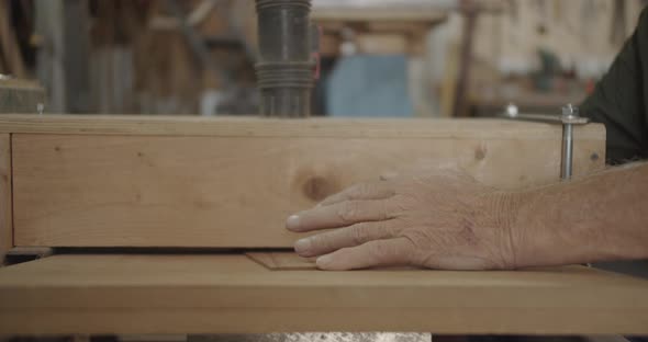 Old man hands pushing thin wood into a filer
