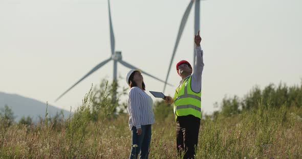 The Client and the Engineer Look at the Tablet To Order. The Customer Points To the Windmills in the alt