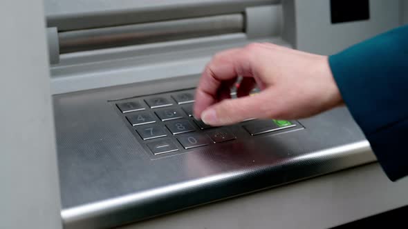 A woman is typing a PIN security code on the keyboard of a modern ATM. alt