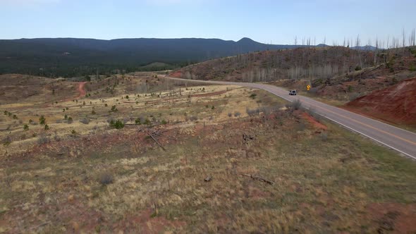 Aerial tracking view of a single vehicle driving along a remote mountain road in the Pike National F alt