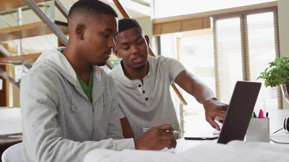 Two african american teenage twin brothers using a laptop and talking alt