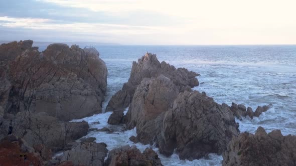 Aerial view over waves breaking onto rocks in the ocean