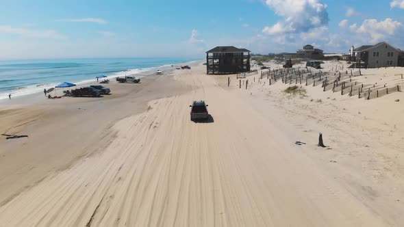 Drone following black suv on Outer Banks Corolla 4x4 beach, houses can be seen inland. alt