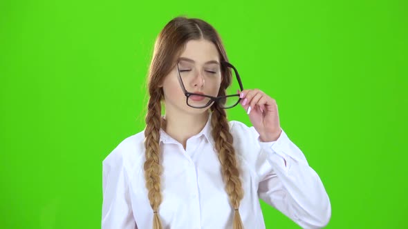 Schoolgirl in a Plaid Skirt Takes Off Her Glasses and Yawns. Green Screen alt