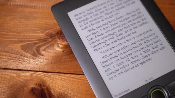 The Electronic Book Lies on a Wooden Table. Screen of Electronic Ink Displays Text of the Book alt
