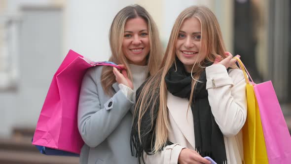 two attractive girls in polto standing on the street of the city hold packages with purchases