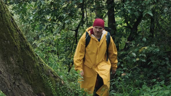 Hiker in a Red Bandana and a Yellow Raincoat Jumps Over a Tree in the Forest alt