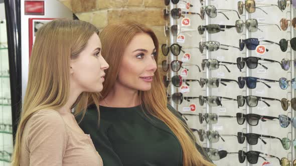 Two Beautiful Young Women Choosing Eyewear in Optician Store alt