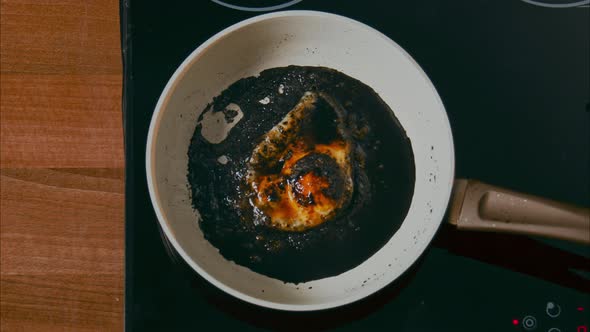 Burnt Egg on a White Pan in Black Oil on a Black Stove