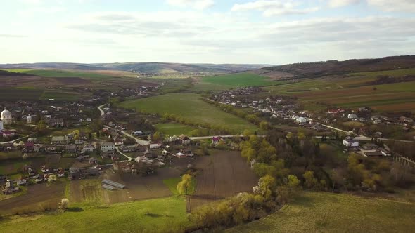 Aerial view of countryside village with small houses among green trees with farm fields alt