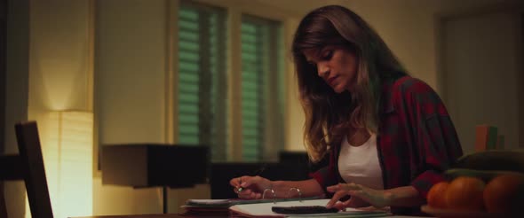 Young woman sitting at desk, studying at home in the evening, calculating math alt