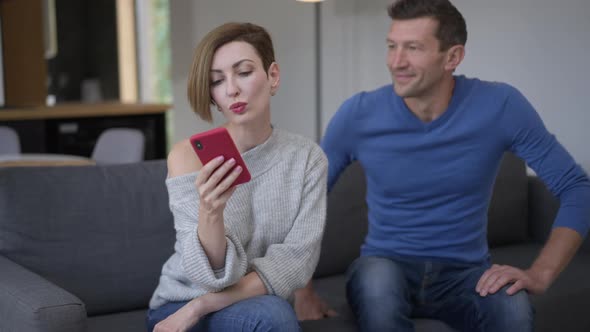 Beautiful Woman Texting on Smartphone Ignoring Man Sitting Down on Couch with Shocked Facial alt