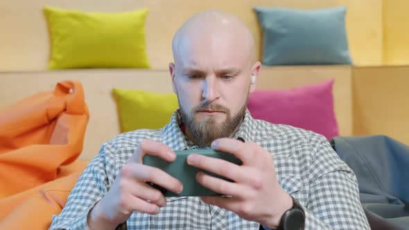 Close Up of an Young Man Sits on a Bean Bag While Playing Online Using His Phone alt