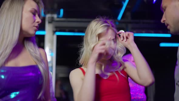 Gorgeous Blond Woman with Blue Eyes in Red Dress Dancing with Group of Friends in Night Club Lights alt