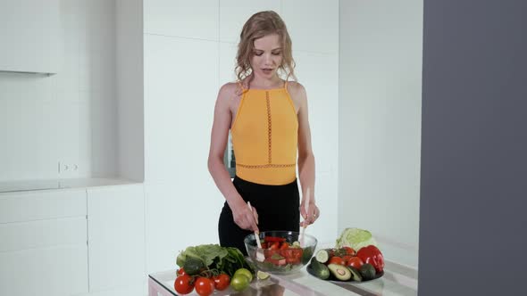 Young Woman Presses Lime Juice On Vegetable Salad. White Modern Kitchen.