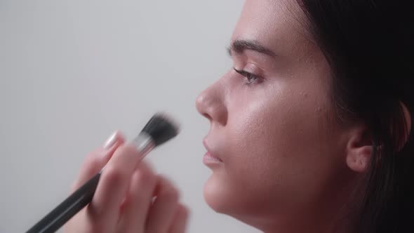 Makeup Artist Applying a Foundation Onto a Female Face As Seen From a Side alt