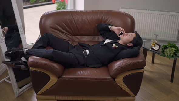 Happy Groom Lying on Armchair Talking on the Phone in Slow Motion alt