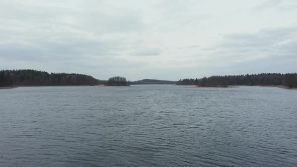 AERIAL: Rippling Water on the Surface of Lake with Forest in Background and Gloomy Sky in Horizon