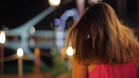 Teenage girl walking along waterfront at night, turning and laughing at camera