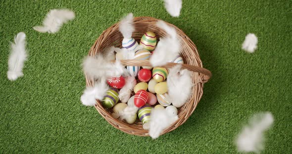 Basket with Many Coloured Eggs on Green Grass Background with White Feathers alt