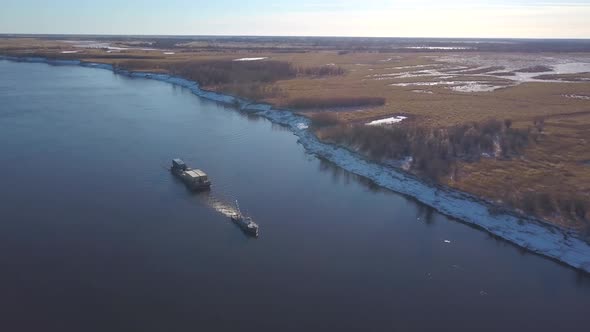 Aerial View of a Barge Floating on a Wide River Past the Autumn Meadows alt