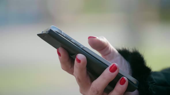 Female Hand with Red Makeup Browsing the Net on a Phone Outdoors in Autumn