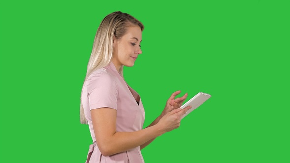 Beautiful woman uses a tablet and walks on a Green Screen alt