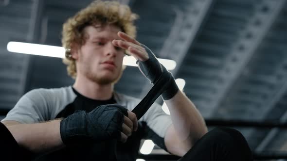 Annoyed Sportsman Using Boxing Tape in Sport Club. Fighter Wrapping Hands at Gym alt