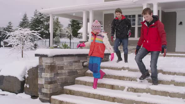 Three kids walking down snowy steps by home in winter
