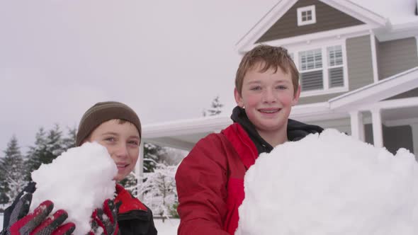 Portrait of two boys holding big snow balls by home in winter