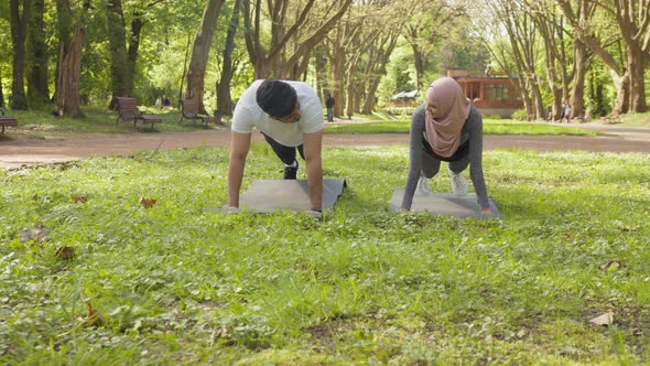 Young Muslim Man and Woman in Hijab and Activewear Standing in Plank Position at alt