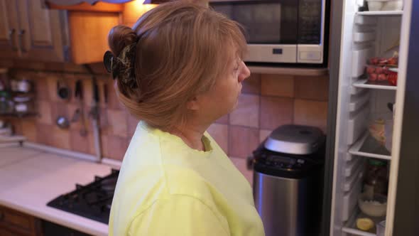 Eating disorder, hungry middle aged woman opens a refrigerator at night and eating unhealthy food. alt