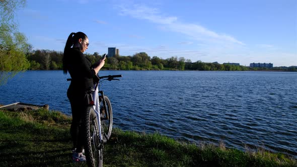 a woman with bicycle walking to lake, river in sunset time. alt