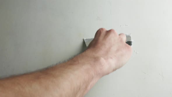 Hand with a spatula smooths out the unevenness of the concrete wall. alt