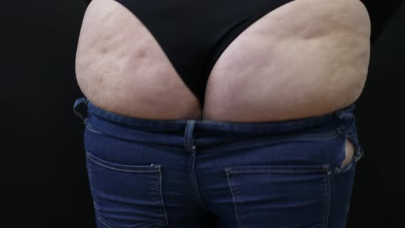 Fat Woman with Cellulite Trying to Put on Jeans on Black Background