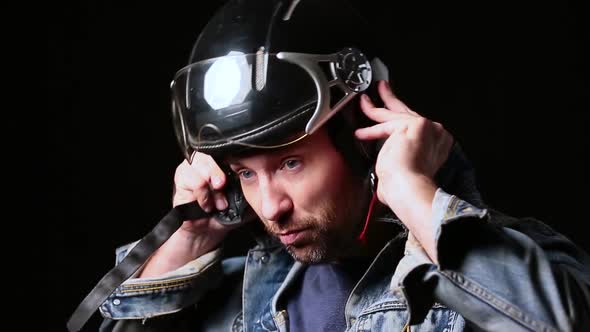 Blue Eyed Bearded Middle Aged Biker Taking on Helmet Over Dark Background. alt
