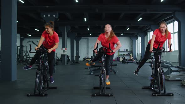 Group of Smiling Friends Women Class Exercising Training Spinning on Stationary Bike at Modern Gym alt