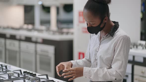 Young Black Woman with Face Mask is Choosing Gas Stove in Home Appliance Stores in Mall Shopping alt
