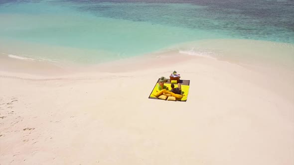 Aerial drone view of a man and woman couple having a picnic meal on a tropical island beach alt