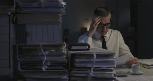 Disappointed businessman working overtime in the office, he is checking paperwork