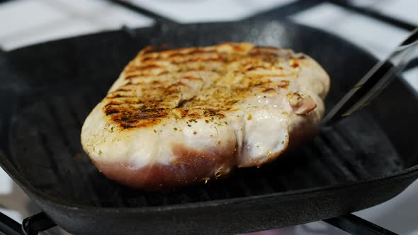Turning Pork Steak On Grill Pan With Kitchen Pliers