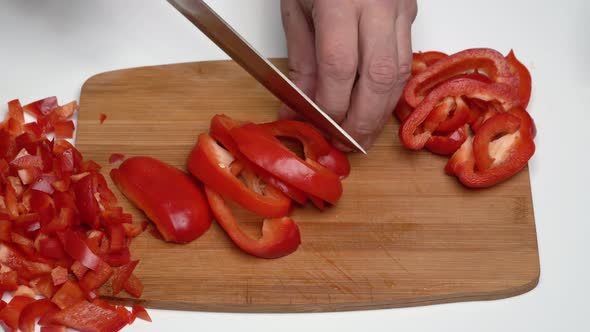 Cook Chopping Red Bell Pepper with Sharp Knife into Small Slices on Wooden Kitchen Cutting Board