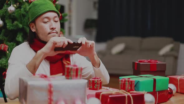 Attractive Asian men using mobile taking photo gift boxes send to friends decorate Christmas tree.