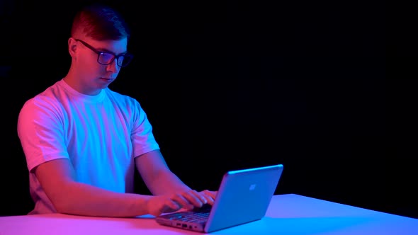 Young Man with a Laptop. A Man Uses a Laptop, Blue and Red Light Falls on a Man on a Black alt