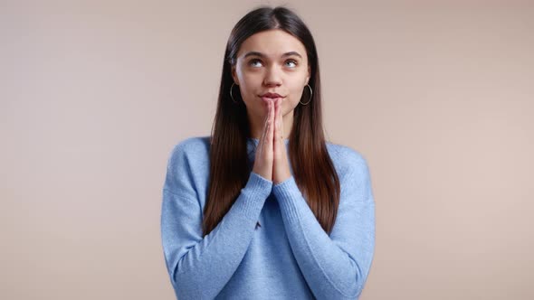 Pretty Woman in Blue Sweater Praying Over Light Background alt
