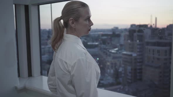 Side View of Confident Mid-adult Businesswoman Looking at Evening City Through Office Window alt