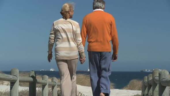 LS OF A SENIOR COUPLE WALKING TO THE BEACH alt