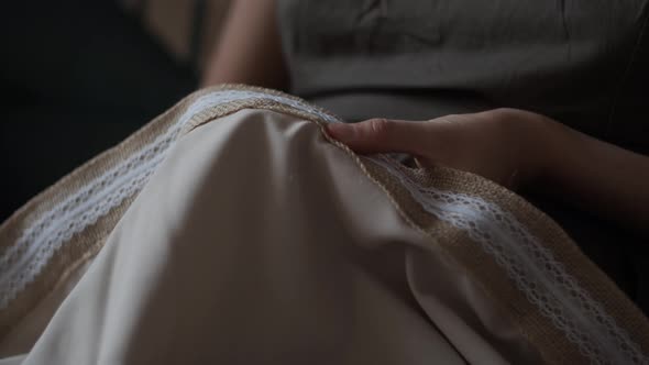Closeup view of female hands sewing  jute linen stripe to beige cotton cloth. Boho rustic home decor alt